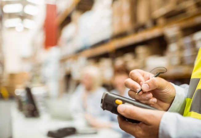 Close up of manager wearing yellow vest using handheld in a large warehouse